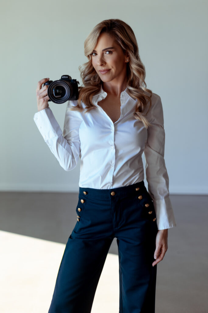 Woman in white blouse holding a Nikon camera, standing and looking at the camera